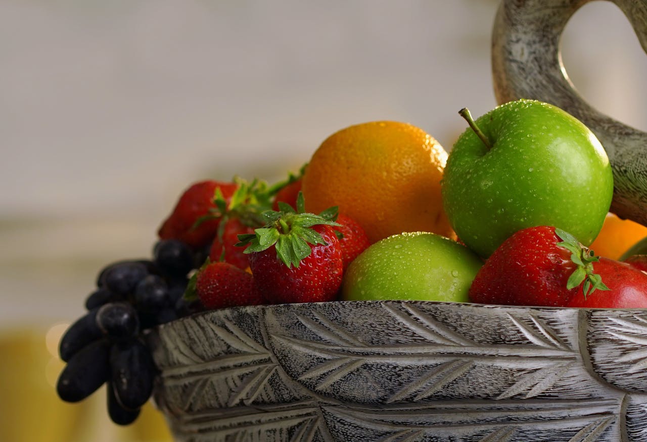 Home Close-up of assorted fresh fruits like apples, oranges, and strawberries in a ceramic bowl.