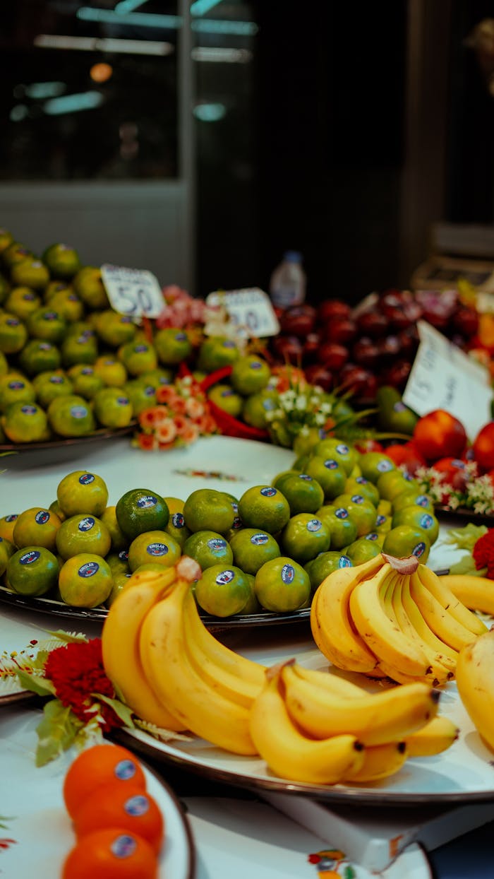 Home A colorful display of fresh fruits including bananas and limes at a bustling market.